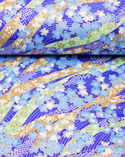 Japanese chiyogami paper featuring blue plum and cherry blossoms with flowing green and brown ribbons on a dark vibrant blue and silver seigaihai background with metallic gold details.