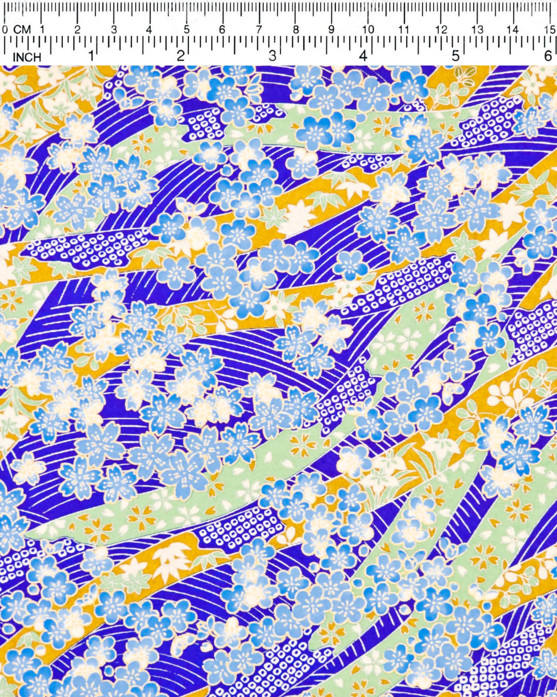 Japanese chiyogami paper featuring blue plum and cherry blossoms with flowing green and brown ribbons on a dark vibrant blue and silver seigaihai background with metallic gold details.