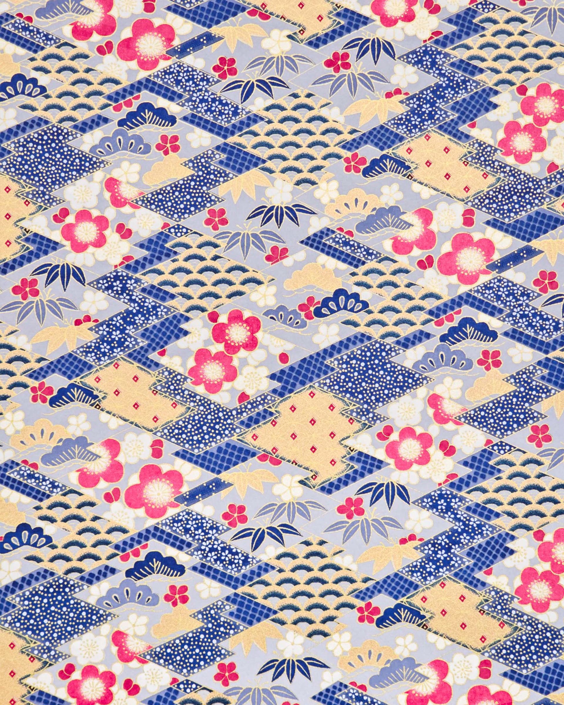 Japanese chiyogami paper featuring large pearlescent magenta pink and white plum blossoms, blue and gold bamboo leaves, and light blue and gold pine on a blue and gold background with metallic gold accents. The background is adorned with a various traditional Japanese geometric designs.