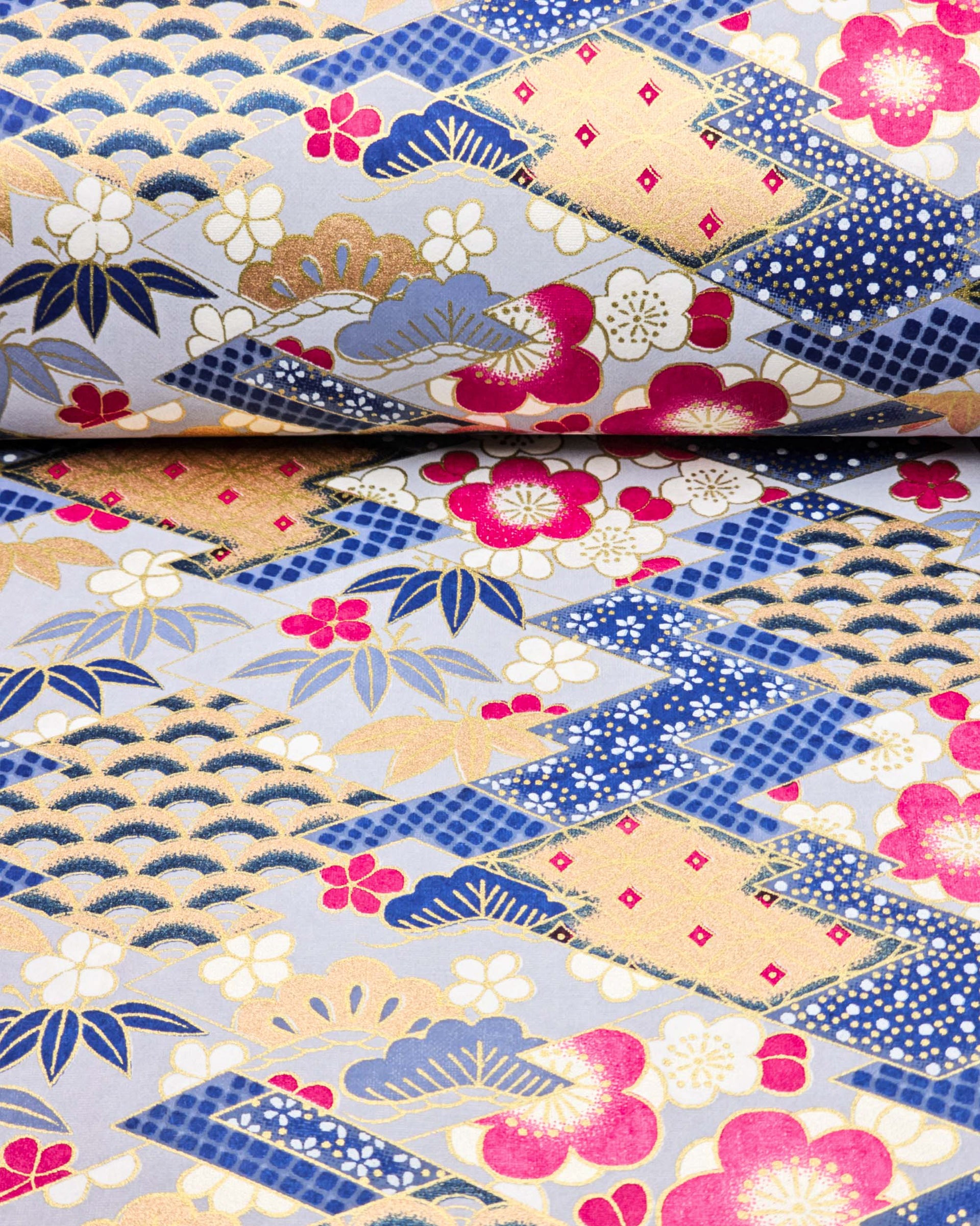 Japanese chiyogami paper featuring large pearlescent magenta pink and white plum blossoms, blue and gold bamboo leaves, and light blue and gold pine on a blue and gold background with metallic gold accents. The background is adorned with a various traditional Japanese geometric designs.