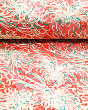 
Japanese chiyogami paper featuring red, green, and white chrysanthemums on a red background with metallic gold details, shown rolled to highlight the design.