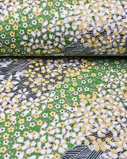 Japanese chiyogami paper featuring white and yellow cherry blossoms on a light green background and a dark green and white wave (aranami) pattern with metallic gold details, and metallic gold details, shown rolled to highlight the design.
