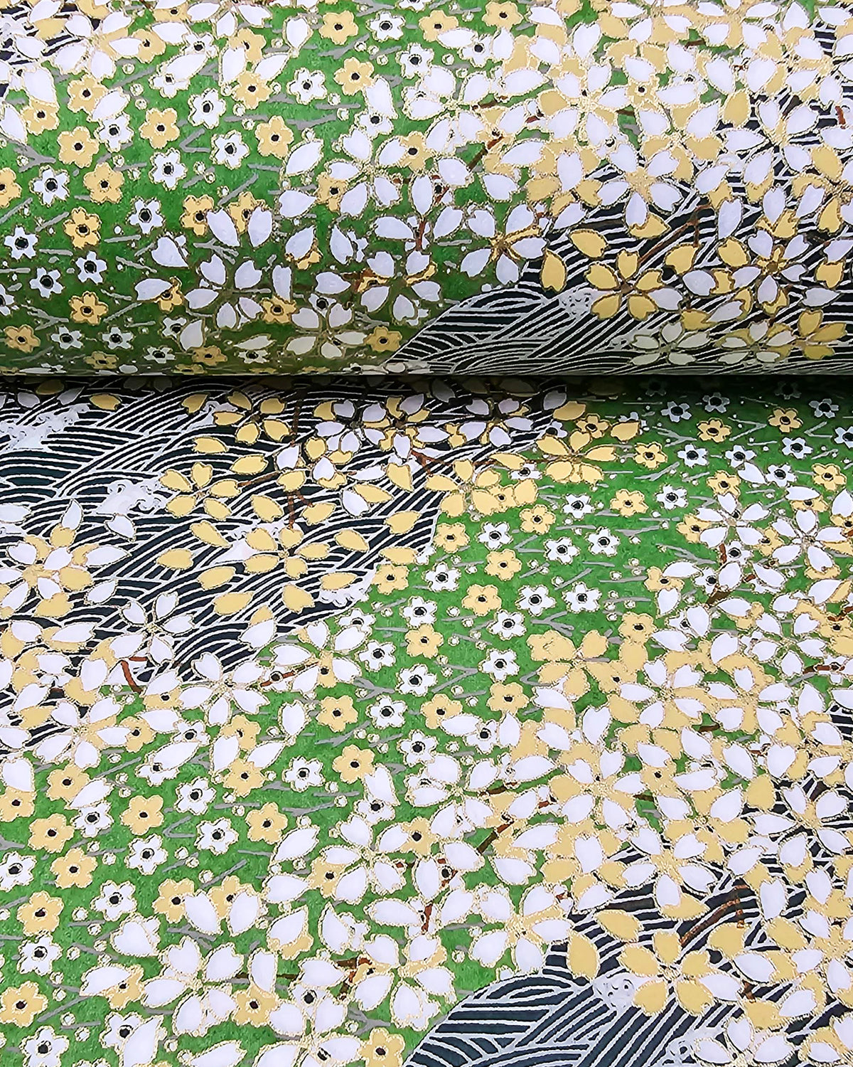 Japanese chiyogami paper featuring white and yellow cherry blossoms on a light green background and a dark green and white wave (aranami) pattern with metallic gold details, and metallic gold details, shown rolled to highlight the design.
