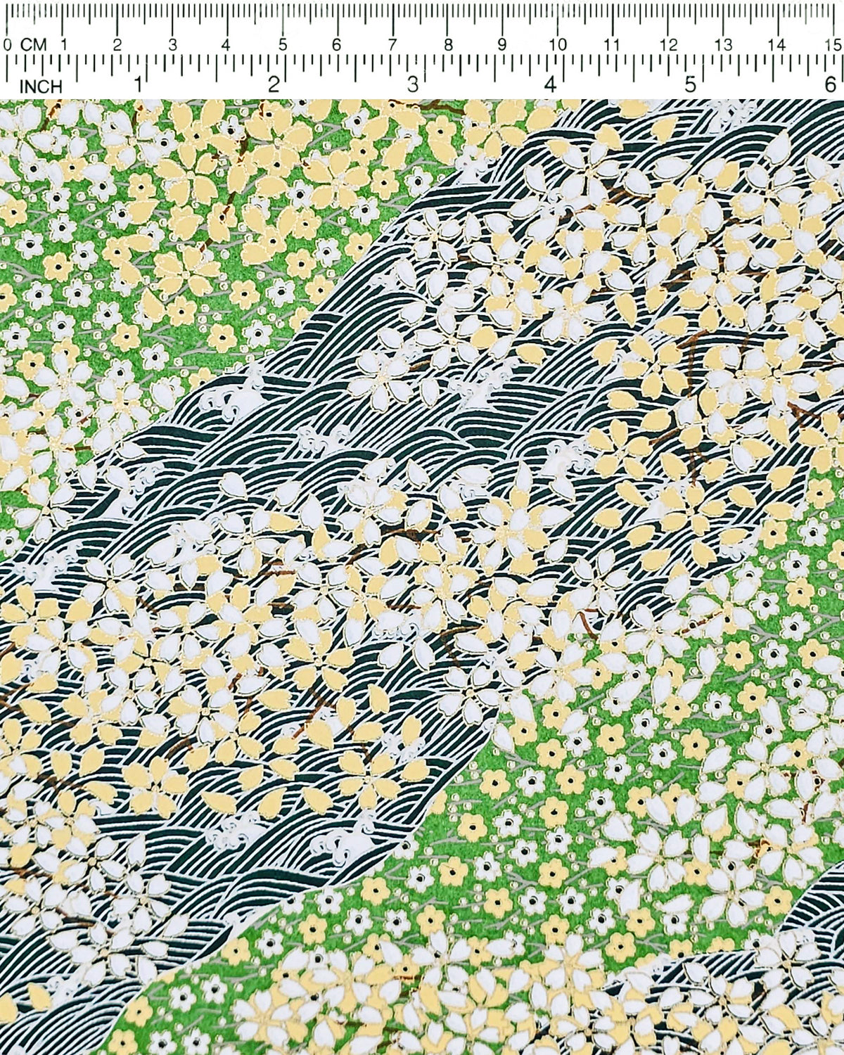 Japanese chiyogami paper featuring white and yellow cherry blossoms on a light green background and a dark green and white wave (aranami) pattern with metallic gold details, and metallic gold details, shown next to a ruler for size reference.