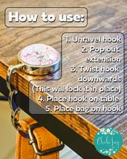 Table-top bag hanger with pink cherry-blossom top hanging from a table, holding a bag, with usage instructions on the image.