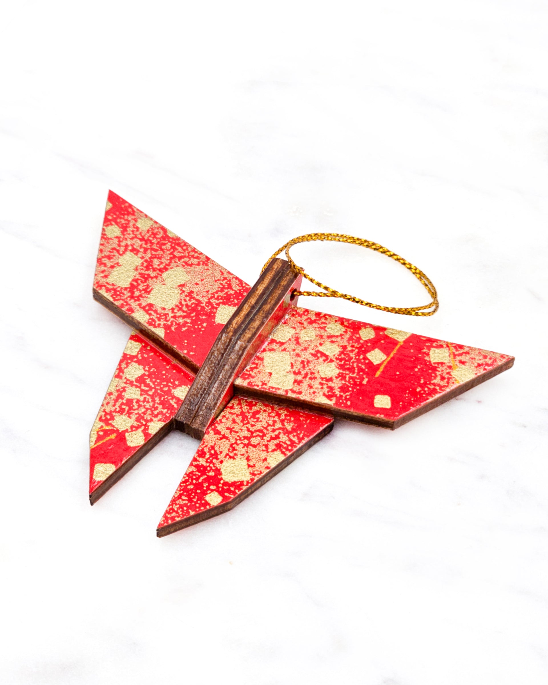 Small wooden origami butterfly ornament featuring scattered metallic gold geometric shapes and fine gold lines on a red background.