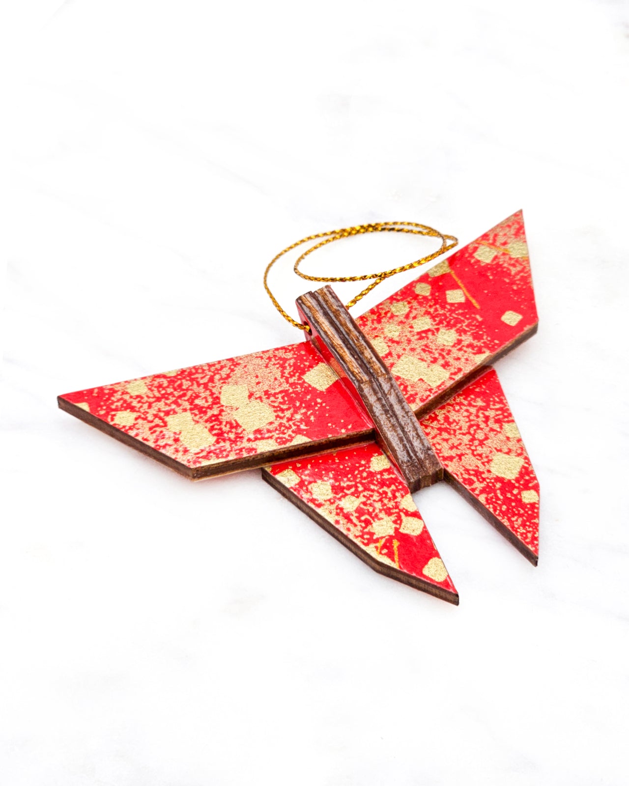 Small wooden origami butterfly ornament featuring scattered metallic gold geometric shapes and fine gold lines on a red background.