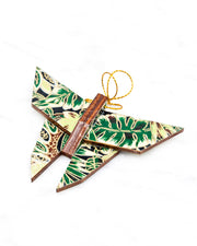 Small wooden origami butterfly ornament featuring green and brown frond leaves on a black background with metallic gold details.
