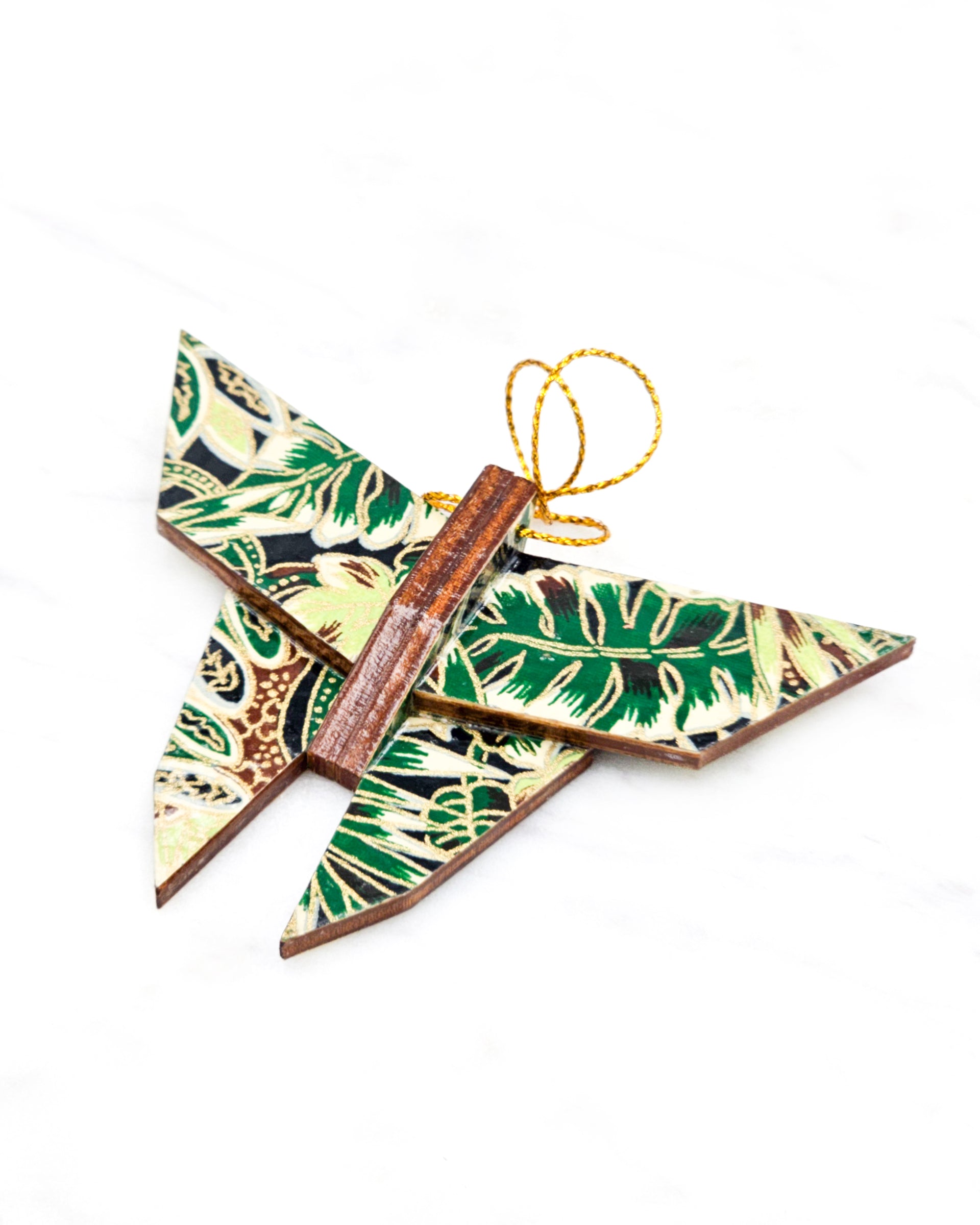 Small wooden origami butterfly ornament featuring green and brown frond leaves on a black background with metallic gold details.
