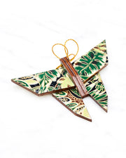 Small wooden origami butterfly ornament featuring green and brown frond leaves on a black background with metallic gold details.