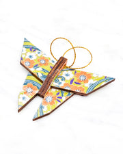 Small wooden origami butterfly ornament featuring orange and white plum blossoms with on a green and blue background with metallic gold details.