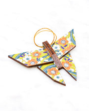 Small wooden origami butterfly ornament featuring orange and white plum blossoms with on a green and blue background with metallic gold details.