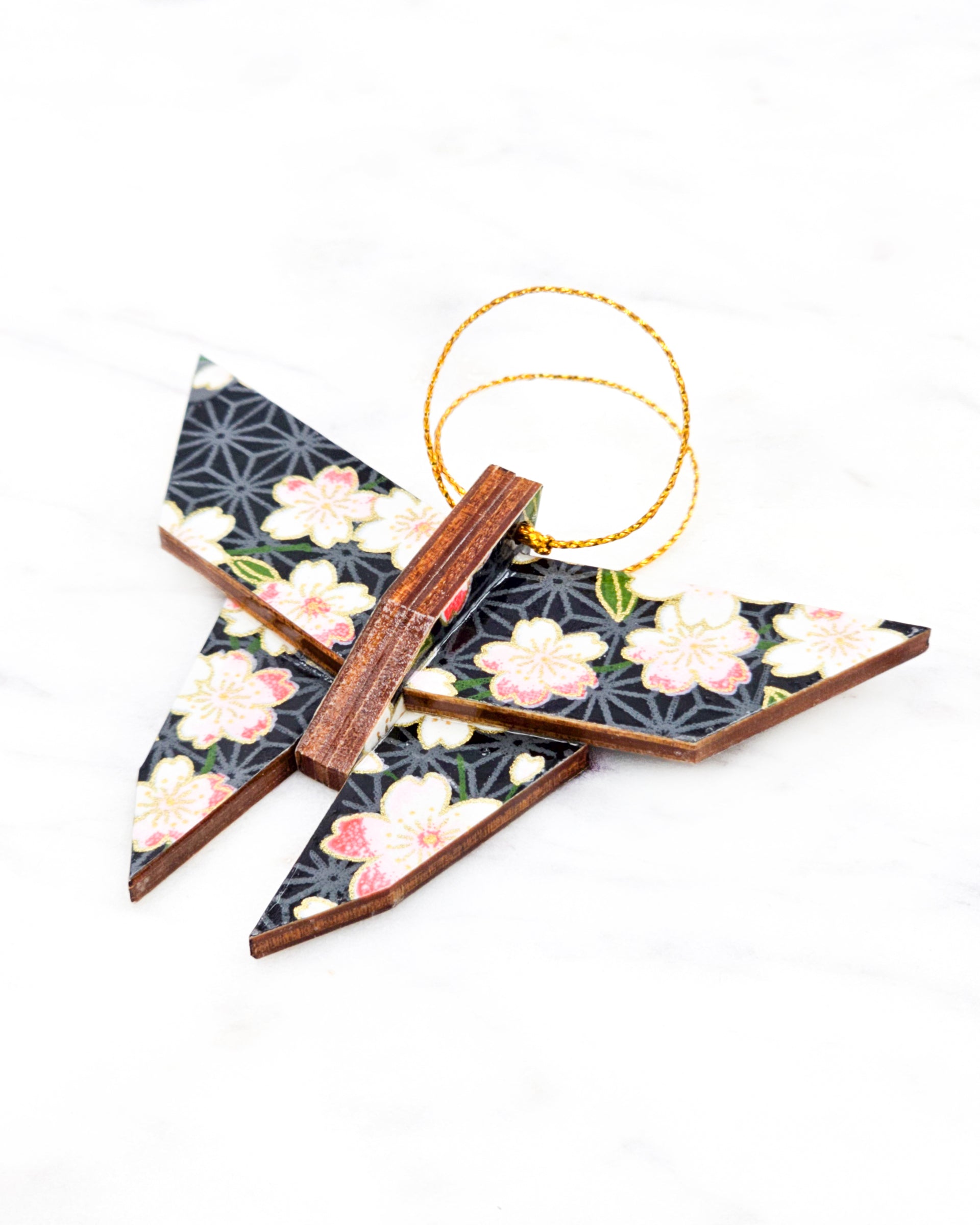 Small wooden origami butterfly ornament featuring pink and white cherry blossoms with green leaves on a black and gray asanoha background with metallic gold details.
