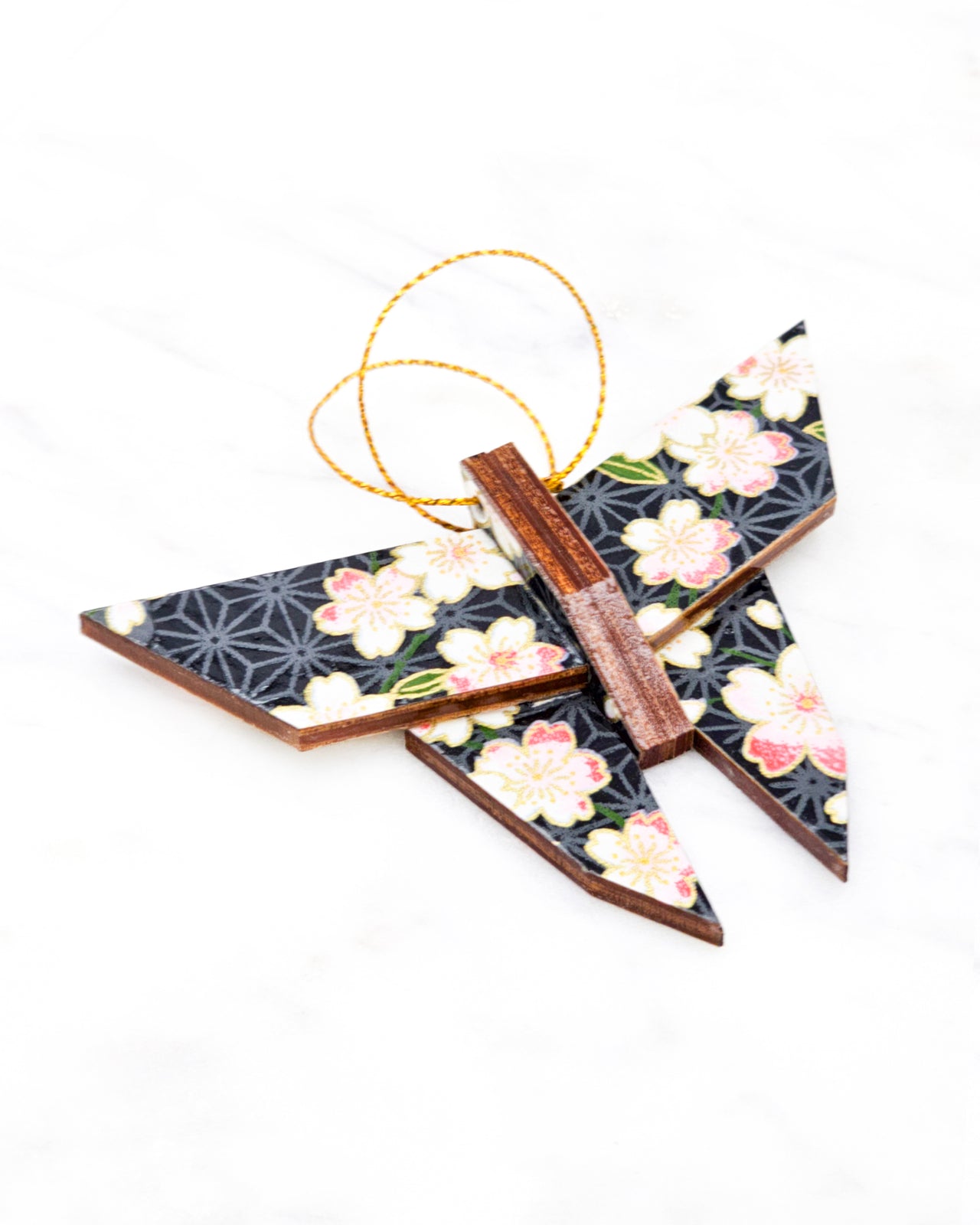 Small wooden origami butterfly ornament featuring pink and white cherry blossoms with green leaves on a black and gray asanoha background with metallic gold details.