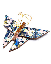 Wooden origami butterfly ornament featuring pink, white, and yellow plum blossoms with pink and blue wisteria on a dark blue background with metallic gold accents.