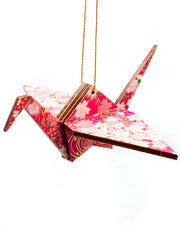 Wooden origami crane ornament featuring pink and white cherry blossoms on a magenta pink background with metallic gold accents.