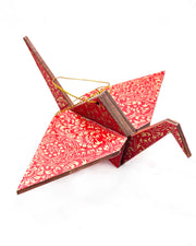 Large wooden origami crane ornament featuring metallic gold filigree circles on a red background.