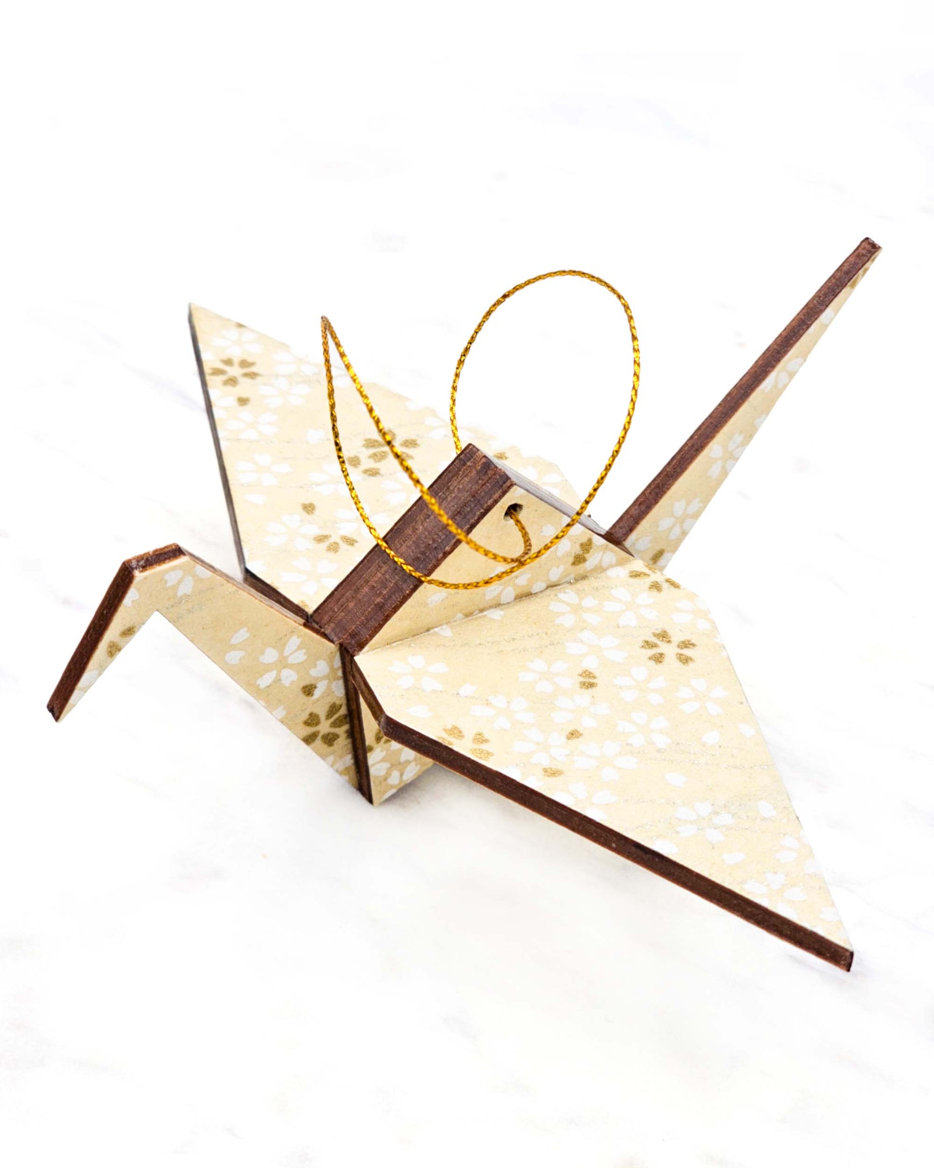 Small wooden origami crane ornament featuring small white and gold cherry blossoms on pearlescent cream background with metallic silver details.