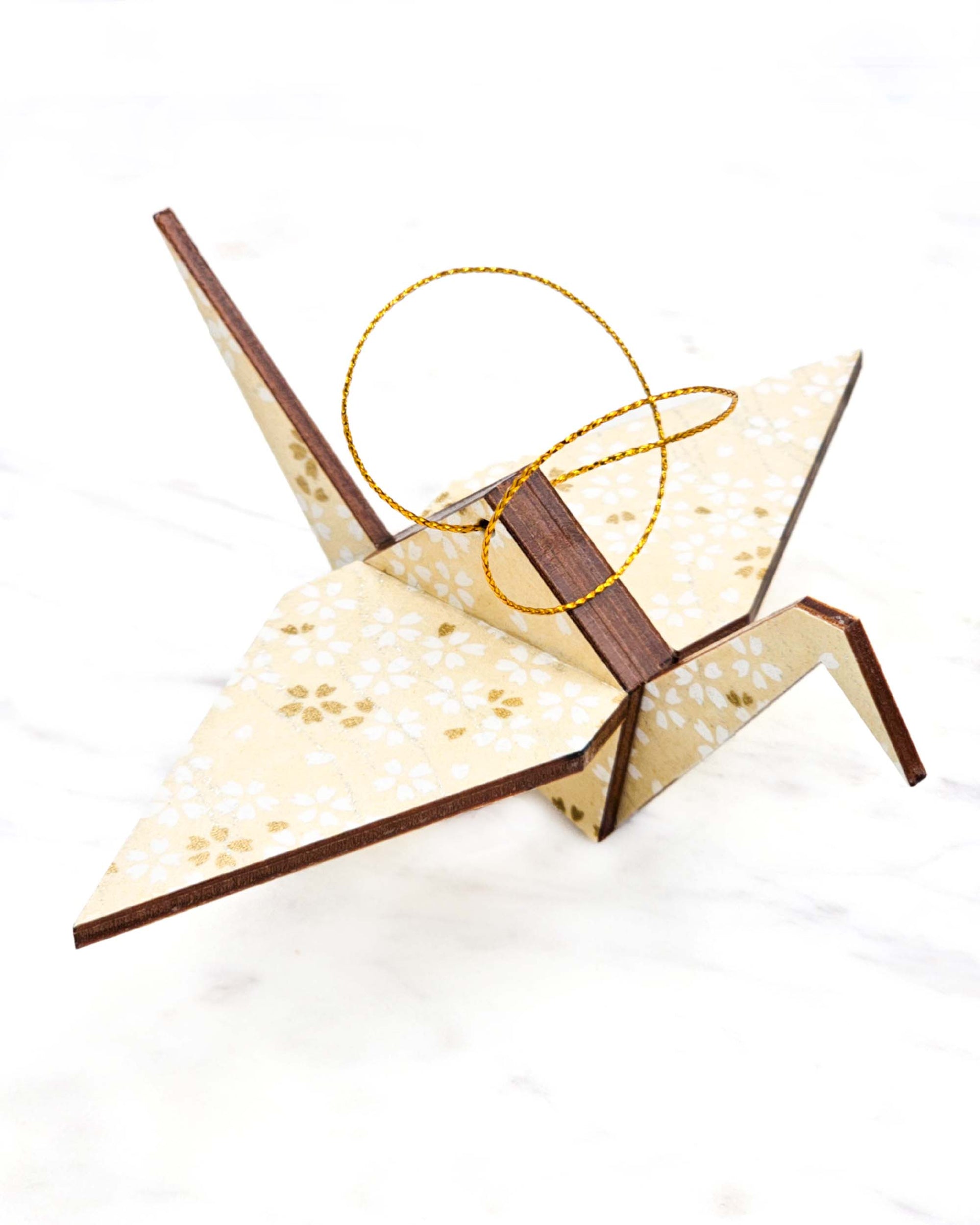 Small wooden origami crane ornament featuring small white and gold cherry blossoms on pearlescent cream background with metallic silver details.