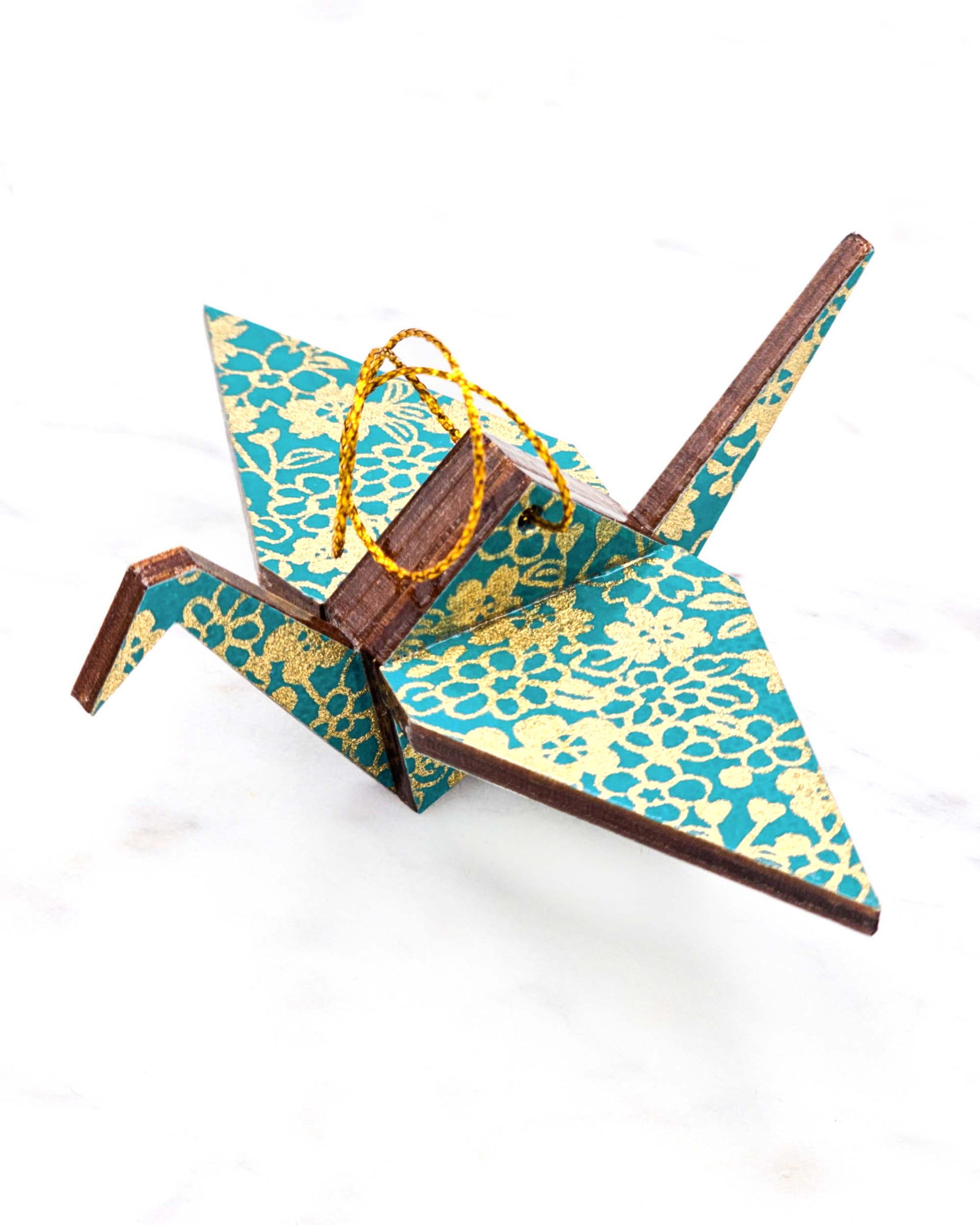 Small wooden origami crane ornament featuring assorted metallic gold flowers on a teal blue background.
