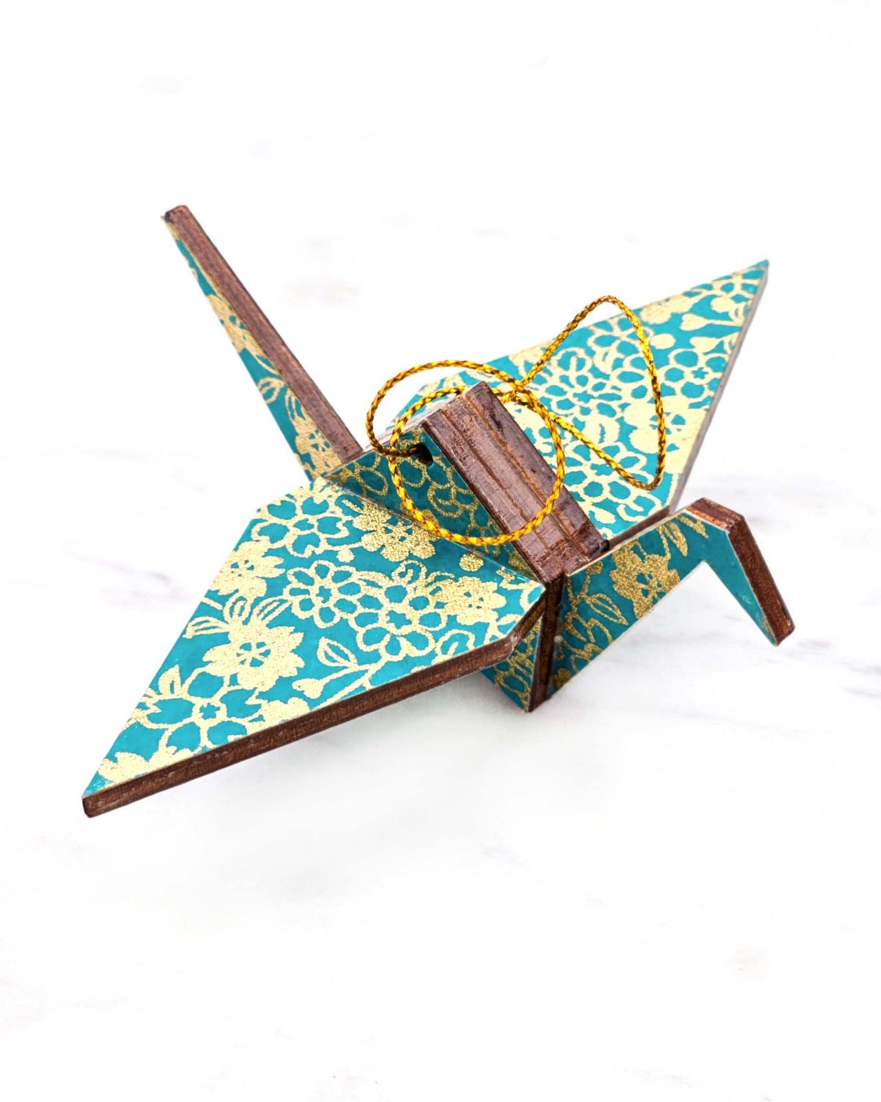 Small wooden origami crane ornament featuring assorted metallic gold flowers on a teal blue background.