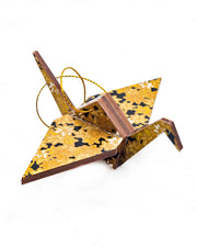 Small wooden origami crane ornament featuring small metallic gold and white momiji (maple leaves) on a black background.