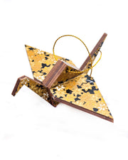 Small wooden origami crane ornament featuring small metallic gold and white momiji (maple leaves) on a black background.