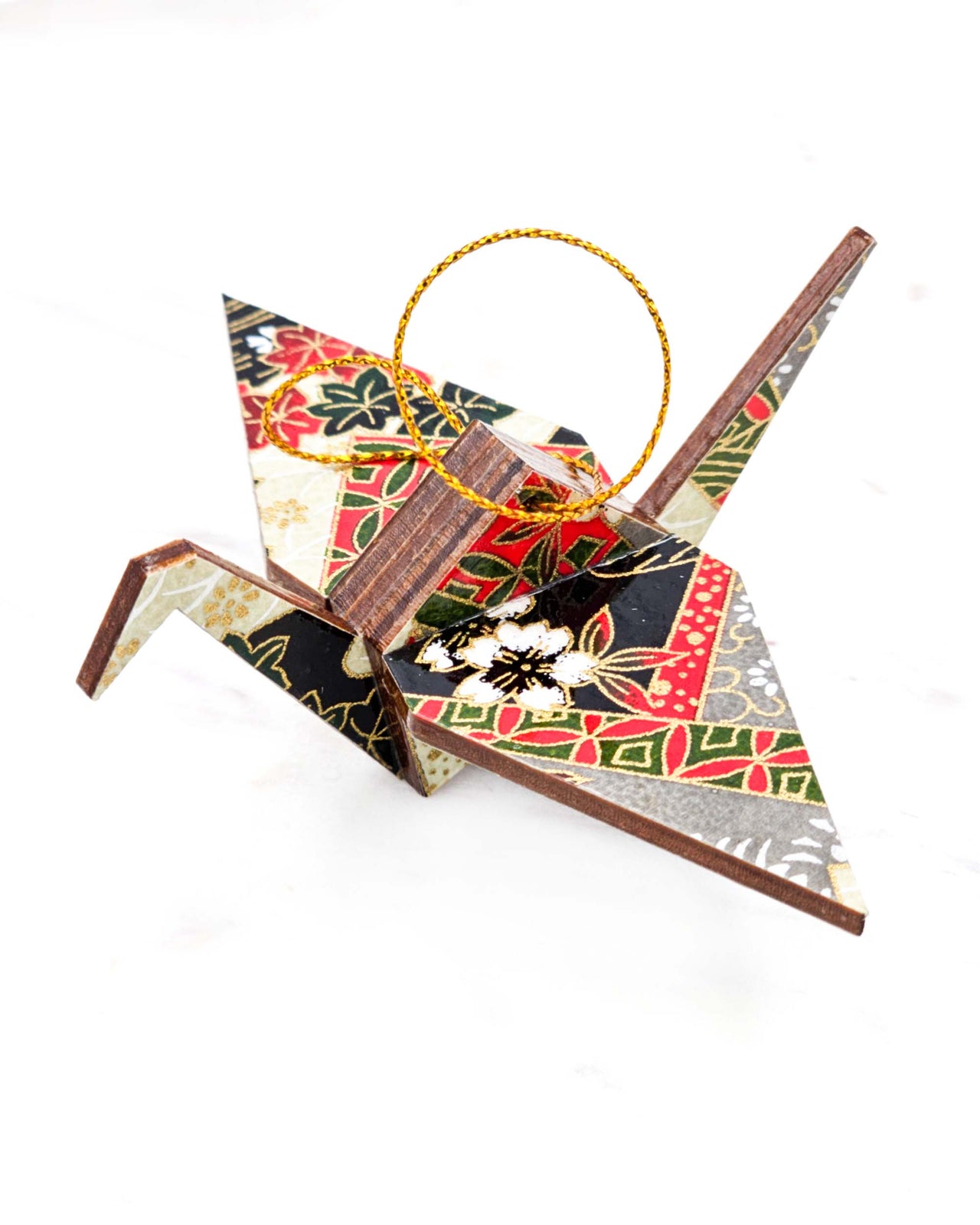 Small wooden origami crane ornament featuring white, black, and red maple leaves and cherry blossoms and red and green shippo patterns on a gray and cream background with metallic gold accents.