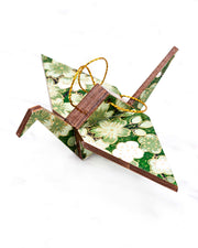 Small wooden origami crane ornament featuring green and white cherry and plum blossoms on a green background with metallic gold accents.