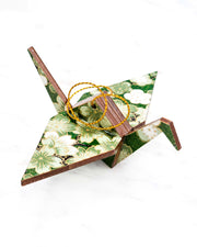 Small wooden origami crane ornament featuring green and white cherry and plum blossoms on a green background with metallic gold accents.