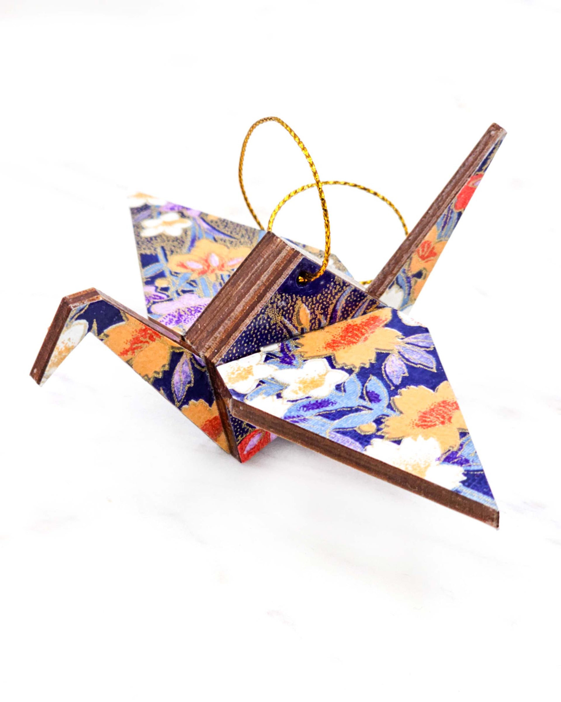 Small wooden origami crane ornament featuring orange, purple, and white irises on a dark blue background with metallic gold accents.