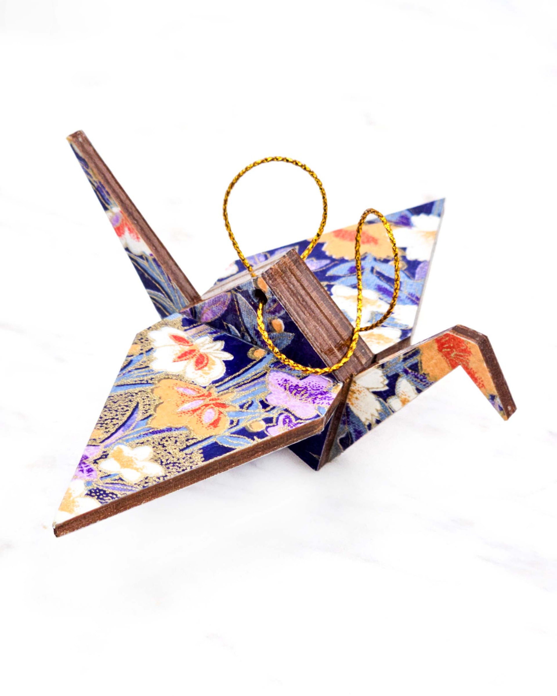 Small wooden origami crane ornament featuring orange, purple, and white irises on a dark blue background with metallic gold accents.