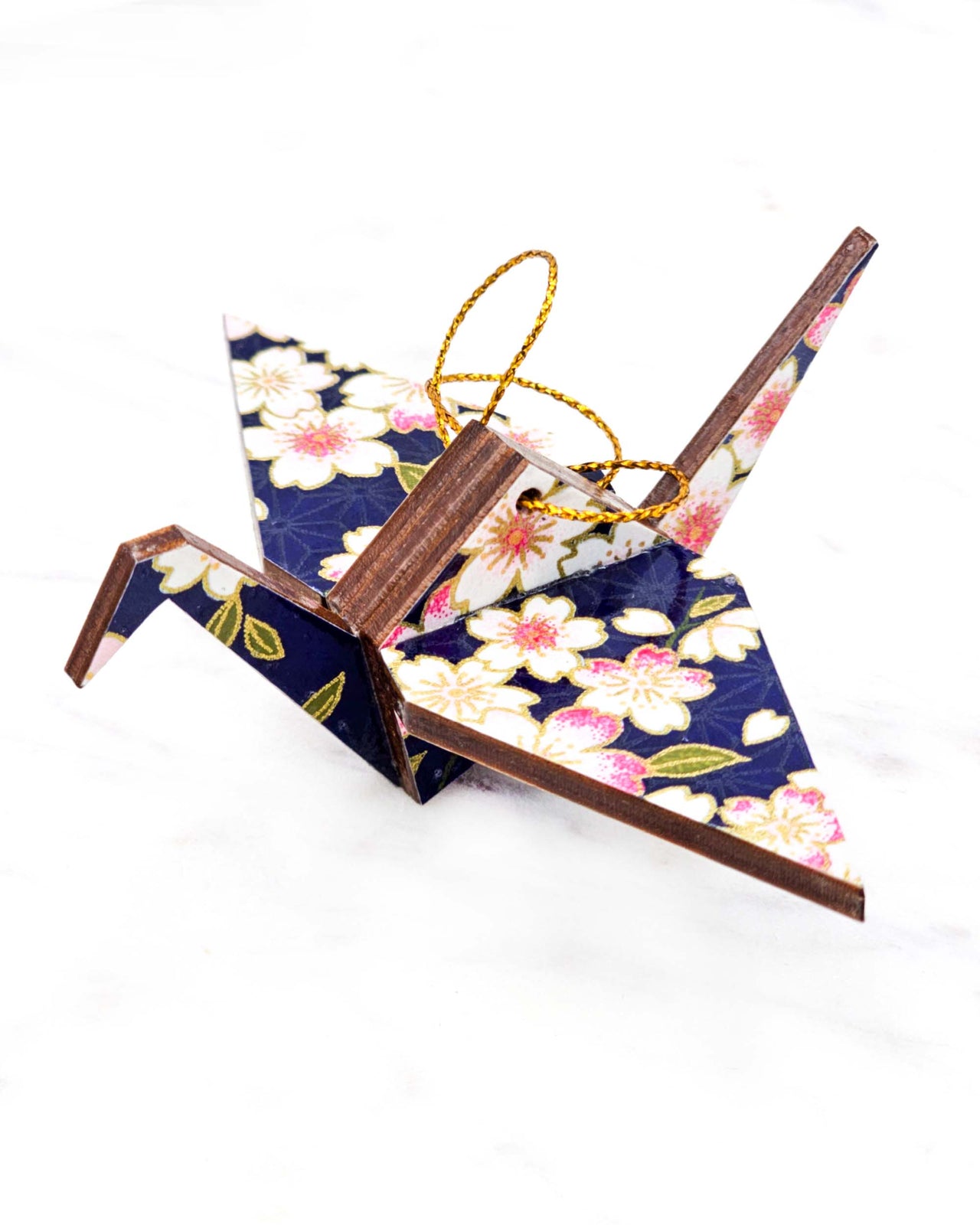 Small wooden origami crane ornament featuring white and pink cherry blossoms on a dark blue background with metallic gold accents.