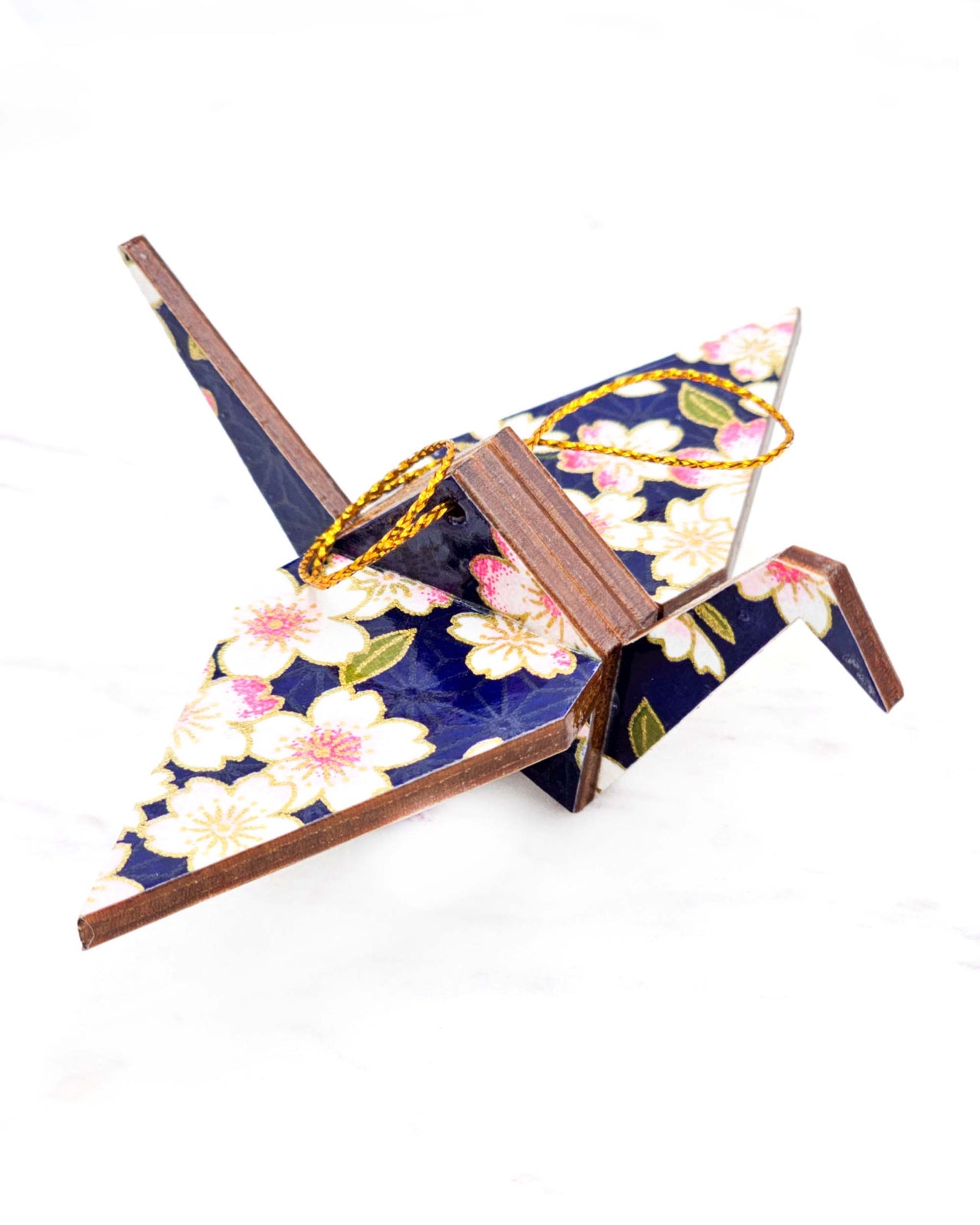 Small wooden origami crane ornament featuring white and pink cherry blossoms on a dark blue background with metallic gold accents.