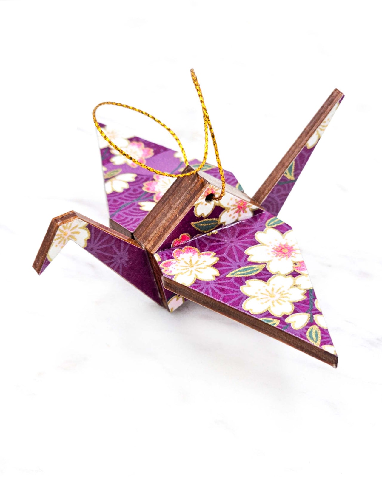 Small wooden origami crane ornament featuring pink and white cherry blossoms on a purple background with metallic gold accents.