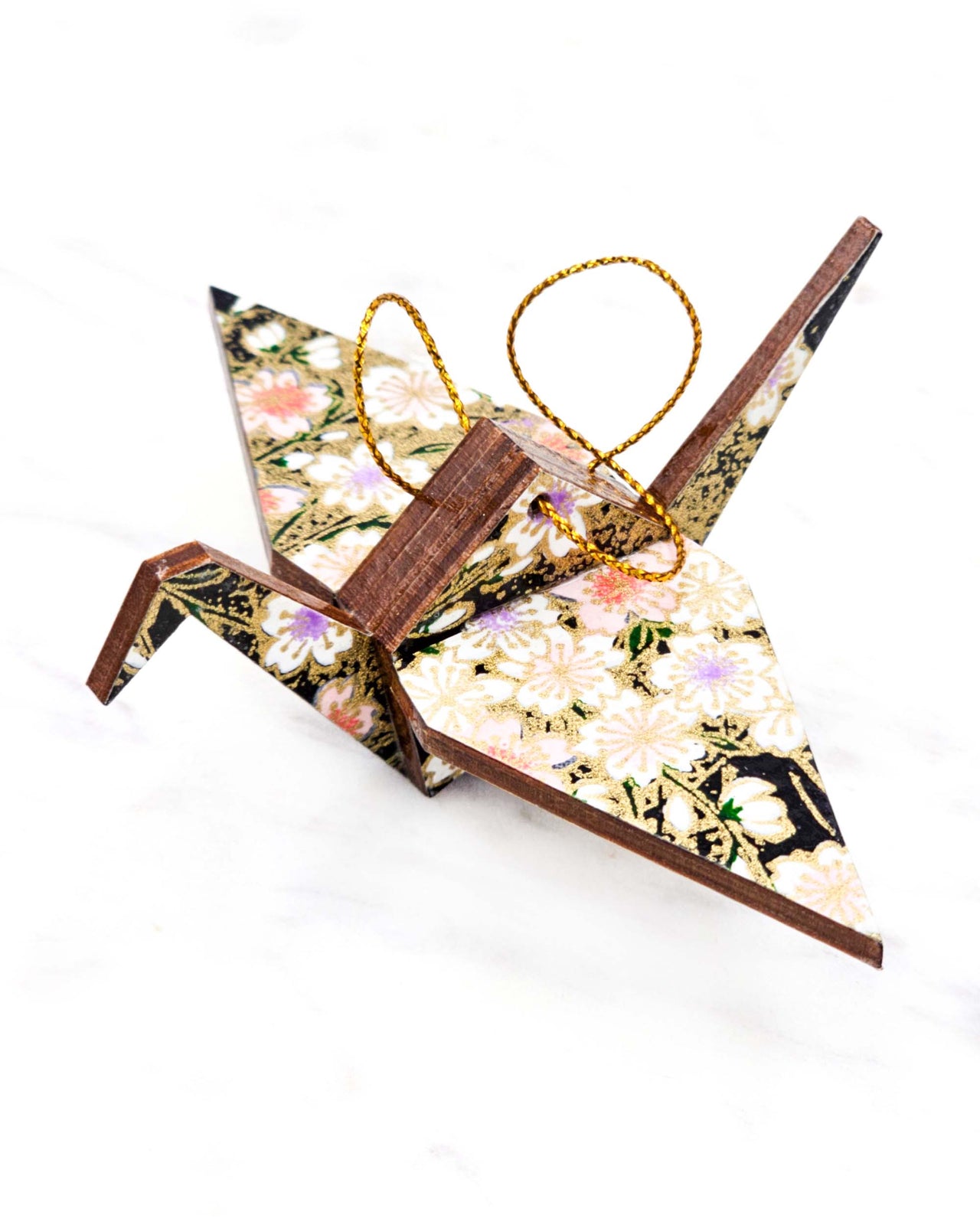 Small wooden origami crane ornament featuring pink, white, and purple cherry blossoms on a black background with metallic gold accents.