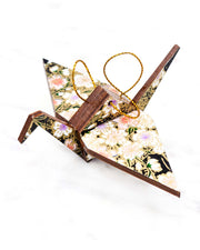 Small wooden origami crane ornament featuring pink, white, and purple cherry blossoms on a black background with metallic gold accents.