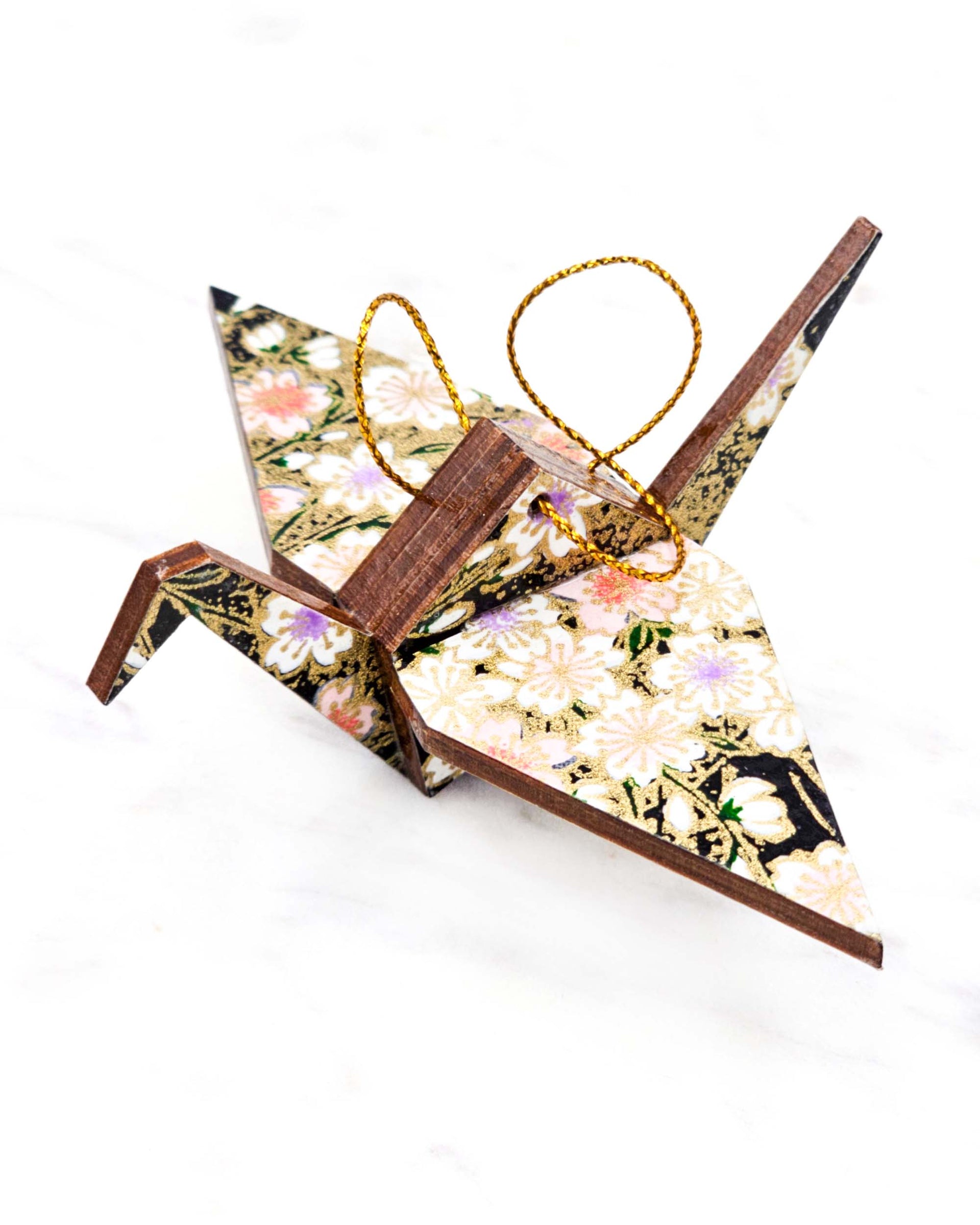 Small wooden origami crane ornament featuring pink, white, and purple cherry blossoms on a black background with metallic gold accents.