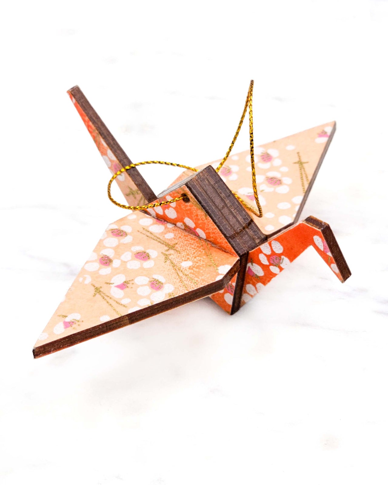 Small wooden origami crane ornament featuring white plum blossoms and gold matsubas on an orange gradient background with metallic gold accents.