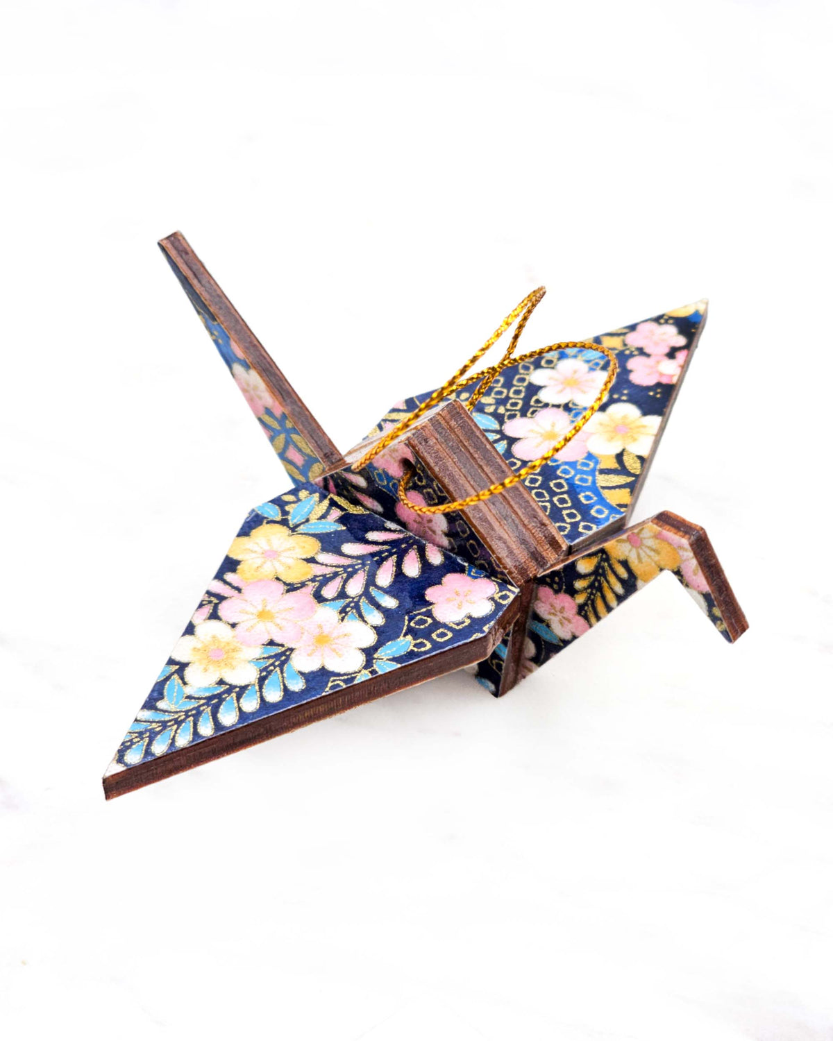 Small wooden origami crane ornament featuring pink and yellow plum blossoms and blue, pink, and yellow wisteria on a dark blue background with metallic gold details.