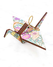 Small wooden origami crane ornament featuring white and pink cherry blossoms on a dark blue background with metallic gold accents.