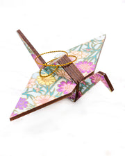 Small wooden origami crane ornament featuring white and pink cherry blossoms on a dark blue background with metallic gold accents.