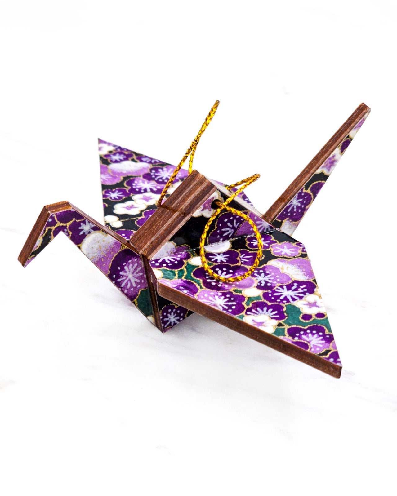 Small wooden origami crane ornament featuring purple and white plum blossoms with green branches on a black background with metallic gold accents.