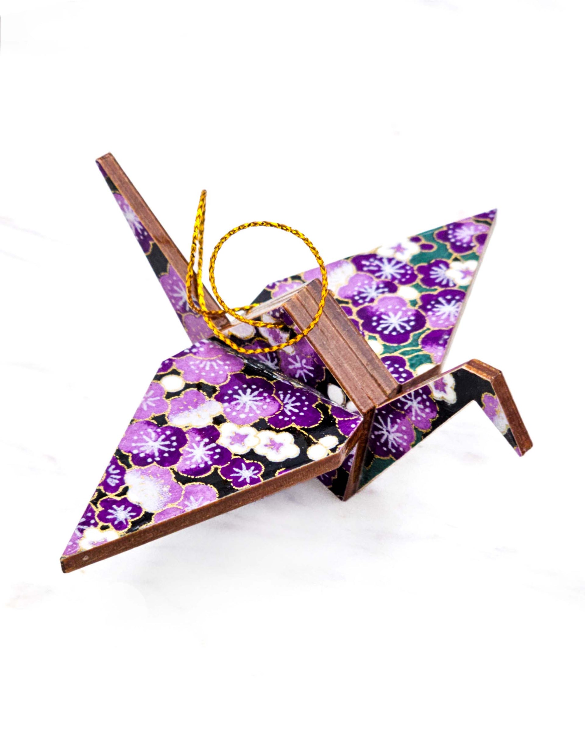 Small wooden origami crane ornament featuring purple and white plum blossoms with green branches on a black background with metallic gold accents.