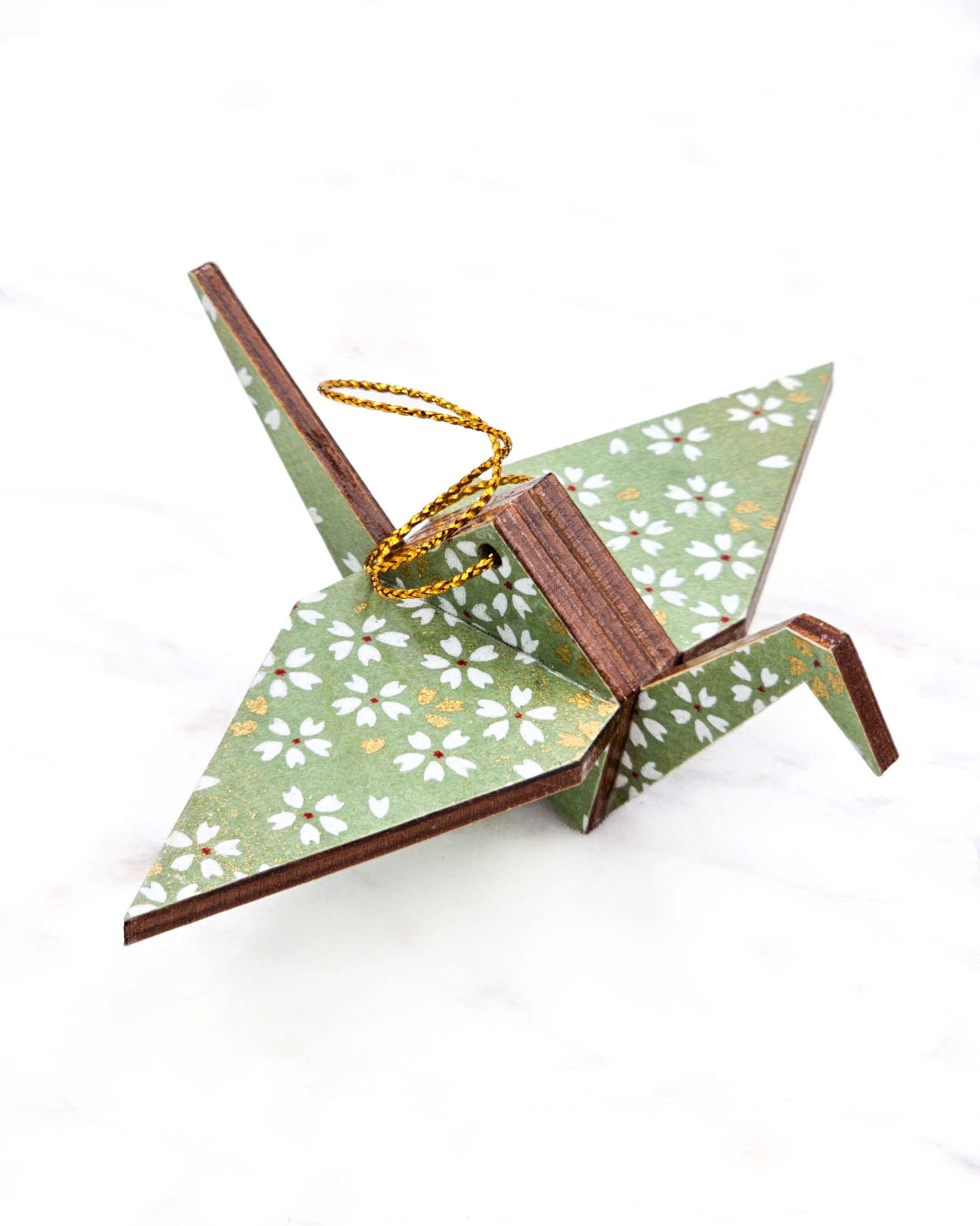 Small wooden origami crane ornament featuring small white and gold cherry blossoms on a light green background with metallic gold details.
