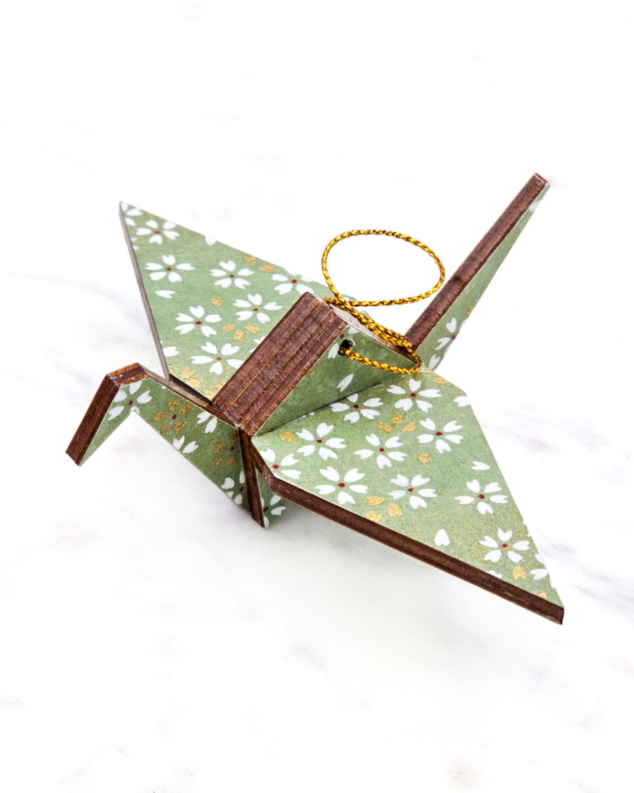 Small wooden origami crane ornament featuring small white and gold cherry blossoms on a light green background with metallic gold details.
