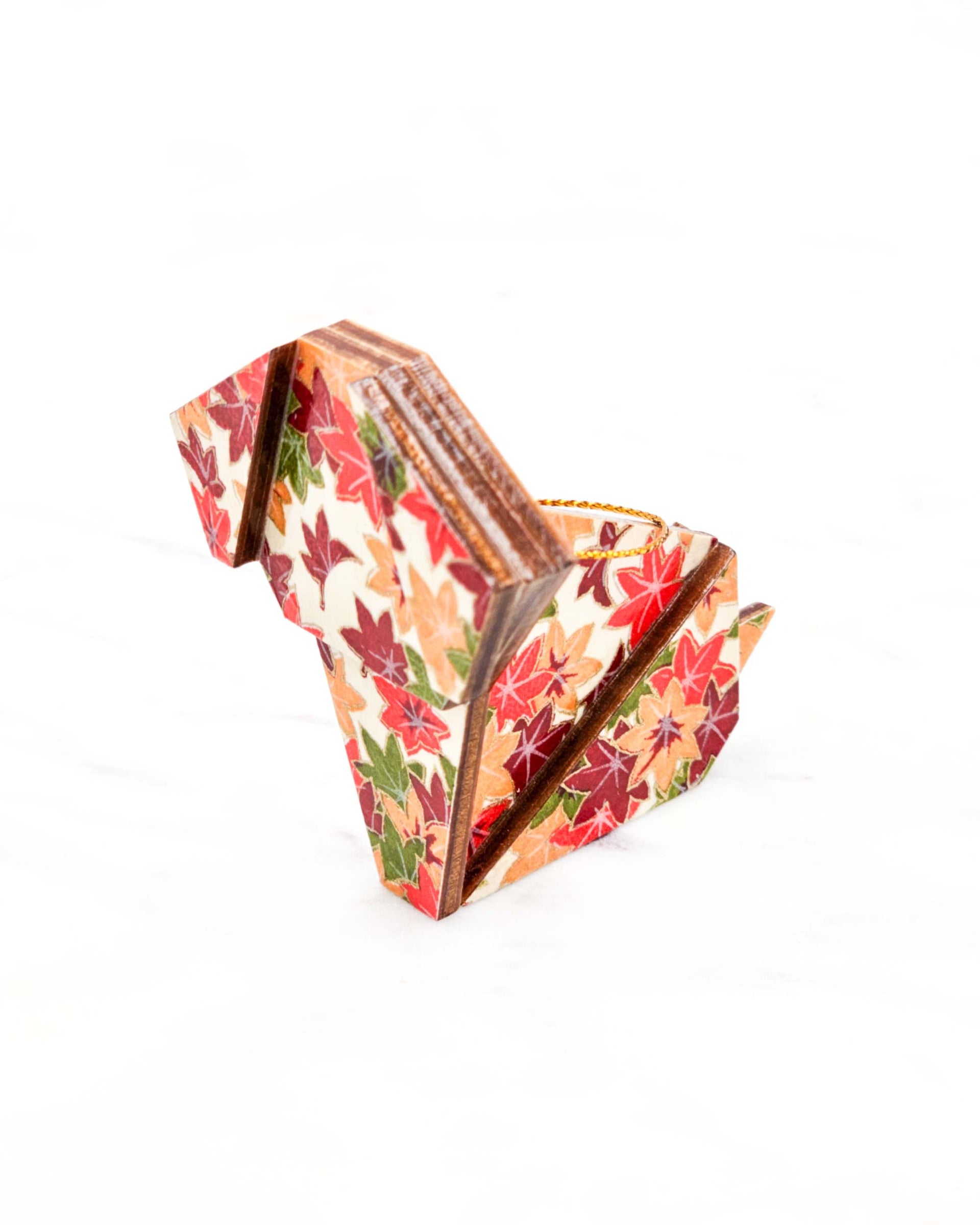 Small wooden origami dog ornament featuring small orange, green, and red Japanese maple leaves on a cream background with metallic gold details.