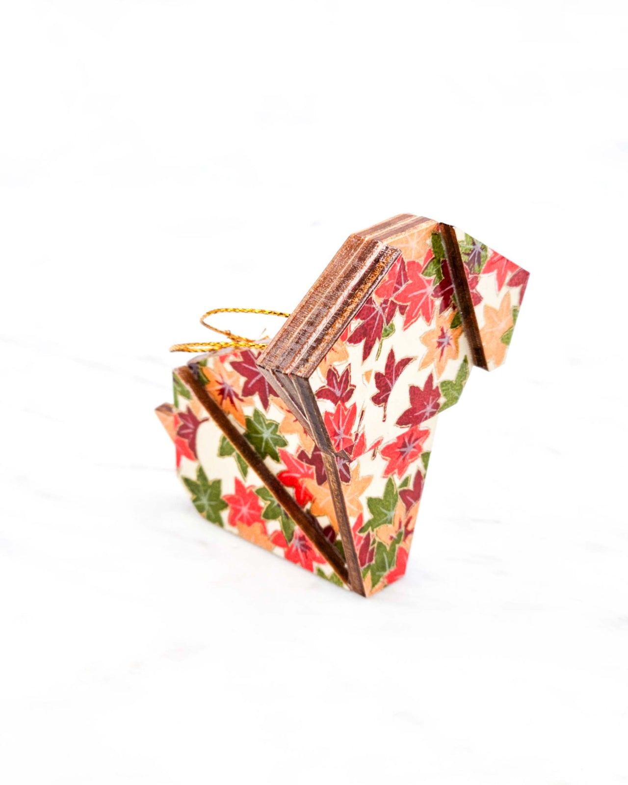 Small wooden origami dog ornament featuring small orange, green, and red Japanese maple leaves on a cream background with metallic gold details.