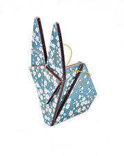 Large wooden origami rabbit ornament featuring small white flower bushes over a blue background with metallic gold details.