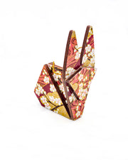Small wooden origami rabbit ornament featuring white plum blossoms with dark brown branches on a maroon red and gold background.
